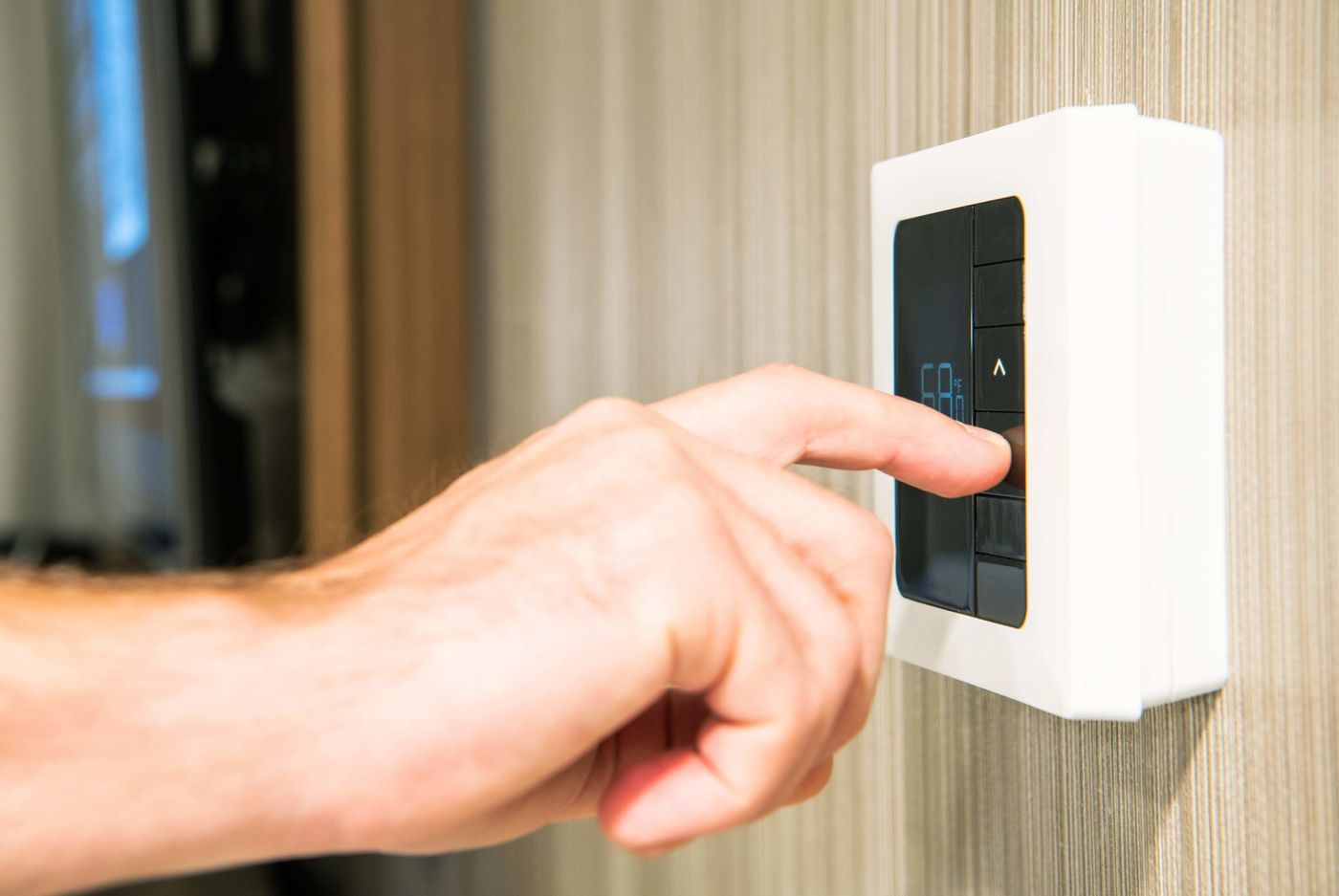 A hand adjusting a wall thermostat